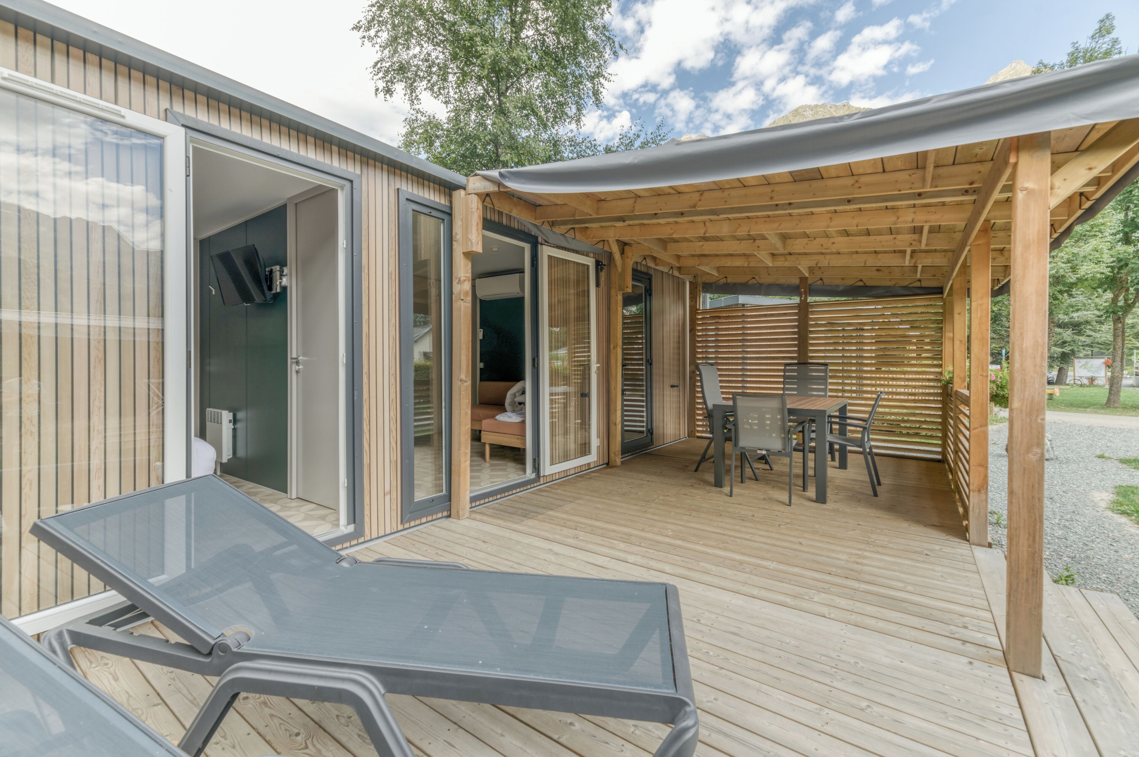 Une terrasse extérieure moderne, dotée d’une porte vitrée donnant sur une pièce, d’une pergola en bois et d’une table avec des chaises.