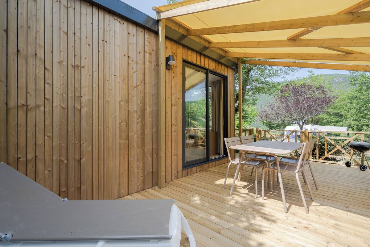 A wooden deck with a table and chairs, a sliding glass door, and a covered area with a grill.
