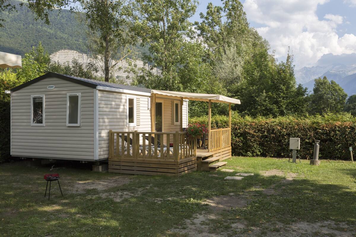 A small, single-story mobile home with a porch and a fenced deck area.