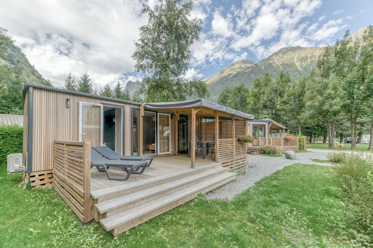 A modern cabin with a deck, large windows, and a mountain backdrop.