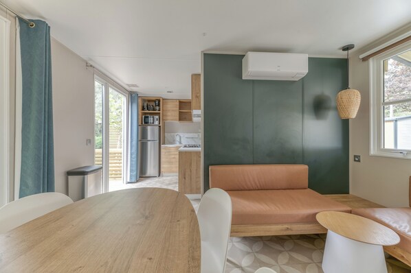 A modern kitchen with a built-in microwave, refrigerator, and wooden cabinets. There is a dining area with a wooden table and a bench. - Camping RCN Belledonne (Le Bourg-d'Oisans)
