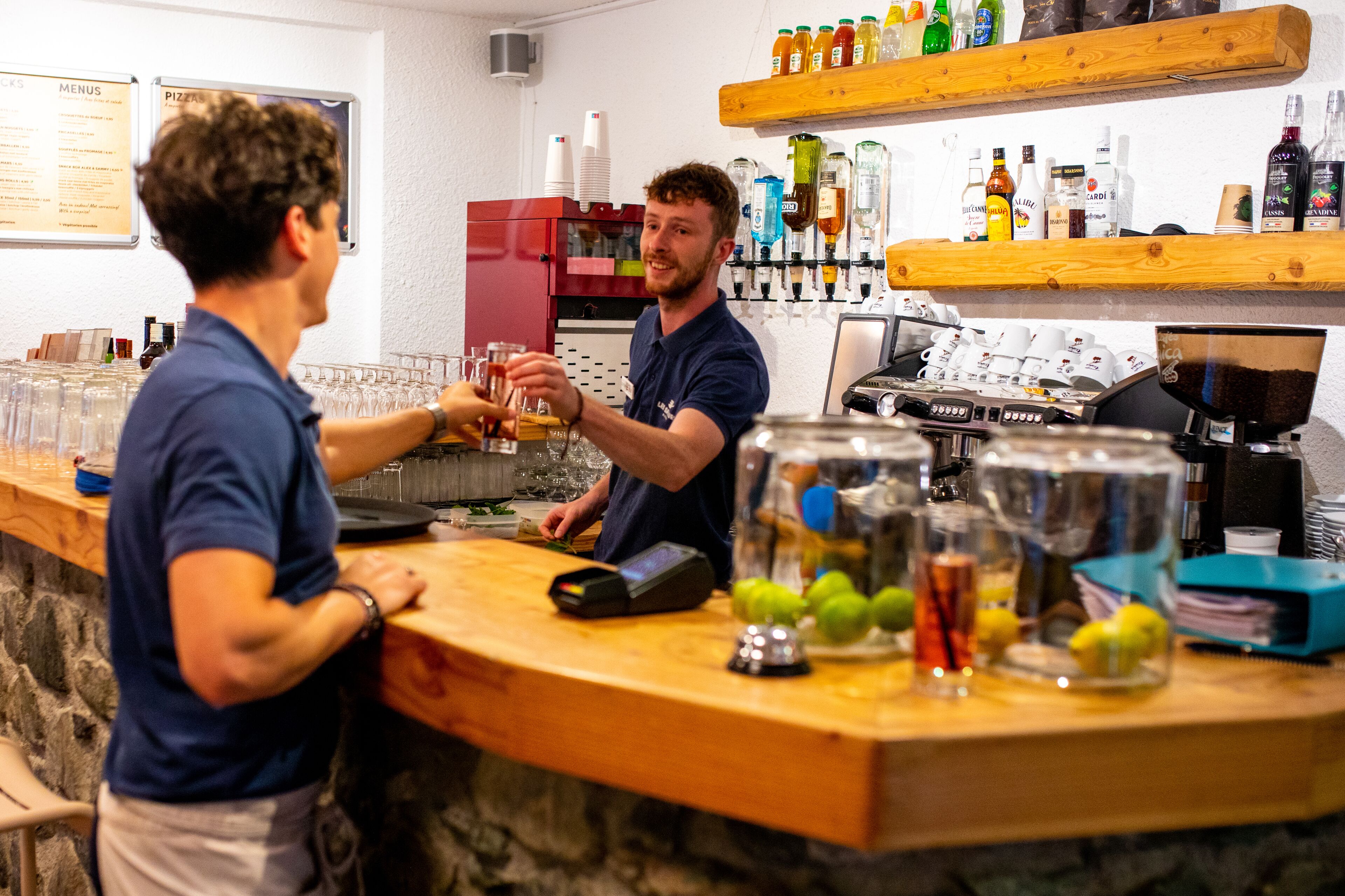 A bar area with a counter, glasses, and bottles.