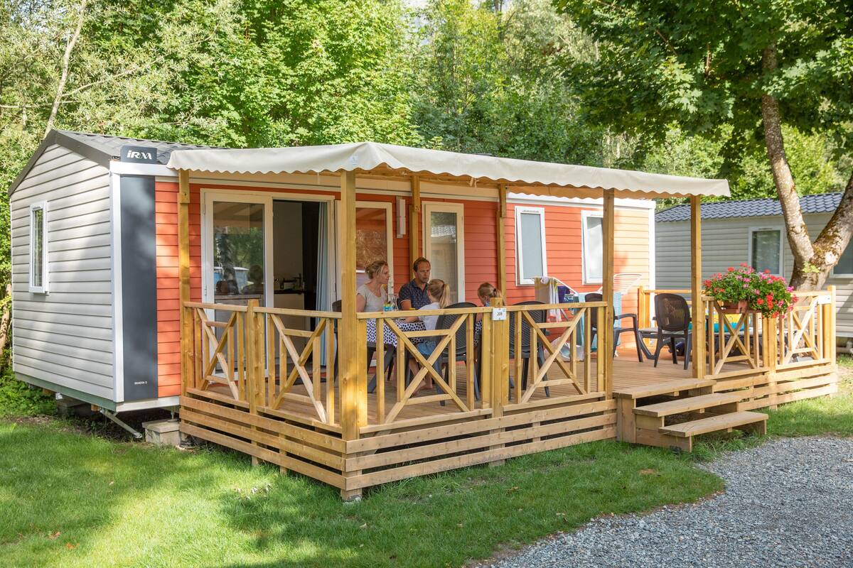 A small, single-story mobile home with a porch, a covered outdoor seating area, and a small garden.