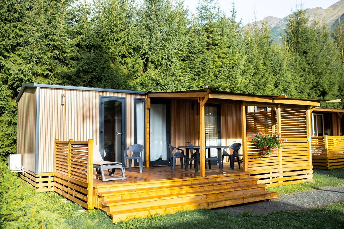 A wooden cabin with a deck, outdoor seating, and a view of a forested area.