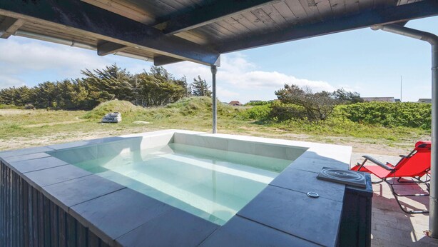 A hot tub under a wooden pergola with a view of a grassy area and trees.