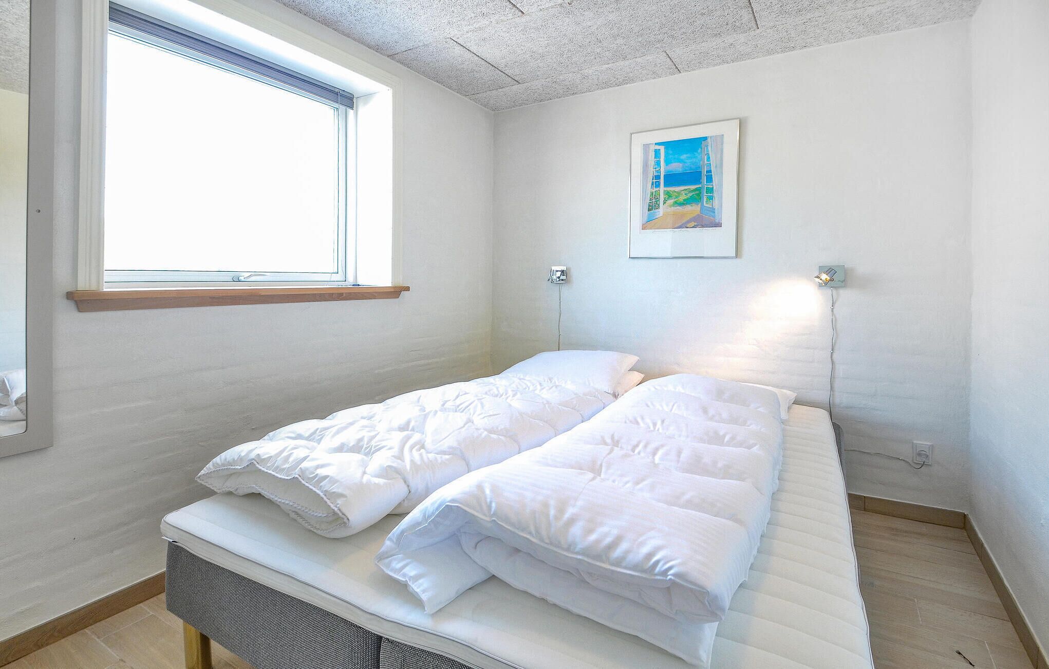 A small, clean room with a single bed, a window, and a painting on the wall.