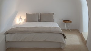 A bedroom with a bed, a bedside table, and a wall-mounted light fixture. - Radiant Santorini (Santorini)