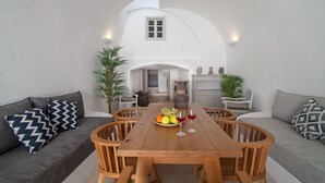 A dining area with a wooden table, chairs, and a sofa with patterned cushions. - Radiant Santorini (Santorini)