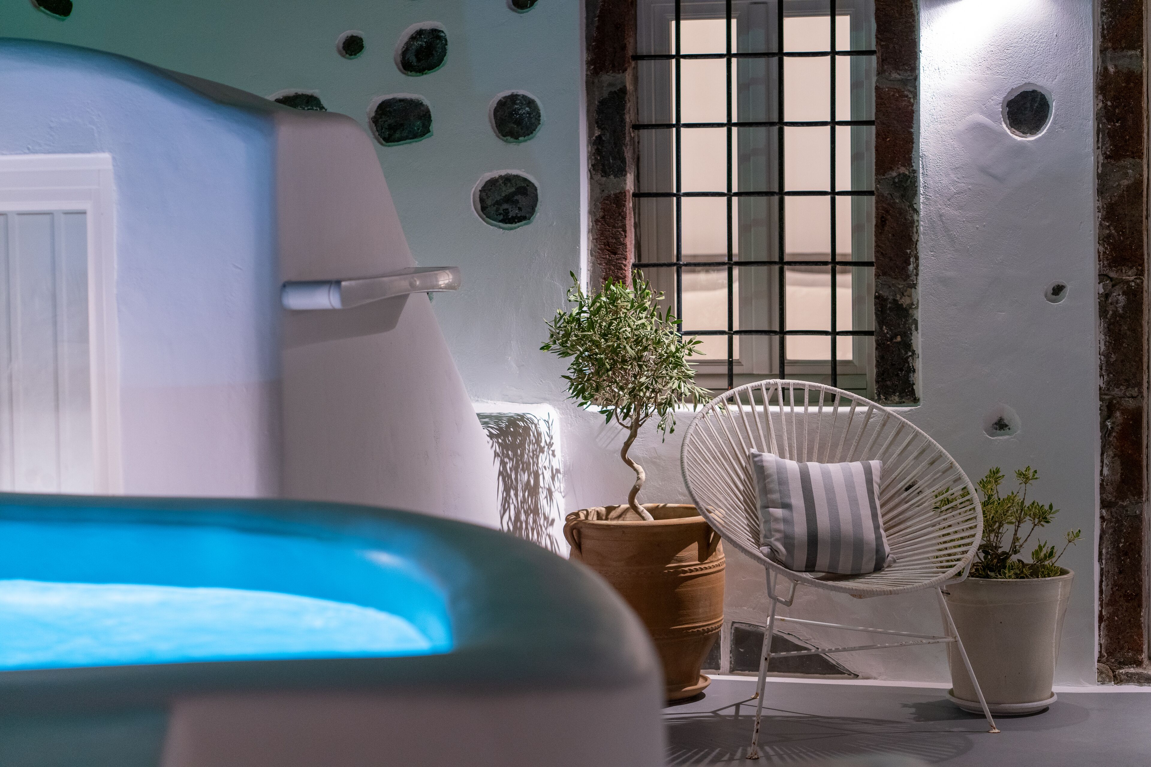 Ein modernes Zimmer mit einer weißen Badewanne, einem Kübelpflanzenbaum, einem weißen Stuhl und einem Fenster mit Gittermuster.