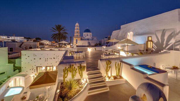 A rooftop terrace with white buildings, a staircase, and a church with a bell tower. - Radiant Santorini (Santorini)