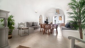 A spacious living area with a sofa, dining table, and chairs, a staircase leading to another level, and potted plants. - Radiant Santorini (Santorini)