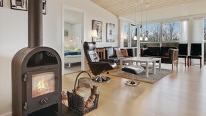 Un salon moderne doté d’un poêle à bois, d’un fauteuil en cuir noir, d’une table basse blanche et d’une grande fenêtre donnant sur l’extérieur.