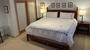 A neatly made bed with white bedding and a wooden headboard, flanked by two bedside tables with lamps, in a room with a door and a small table with a lamp. - Riverdell Condo feature Floor Heating and Gas Grill by RedAwning (Hood River)