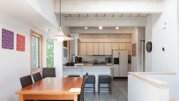A modern kitchen with a central island, wooden dining table, and chairs. - Riverdell Condo feature Floor Heating and Gas Grill by RedAwning (Hood River)
