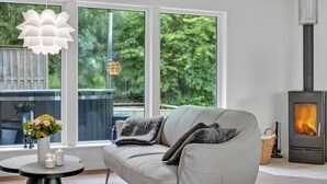 Uma sala de estar moderna com um sofá, uma mesa redonda com velas e uma grande janela com vista para o verde.