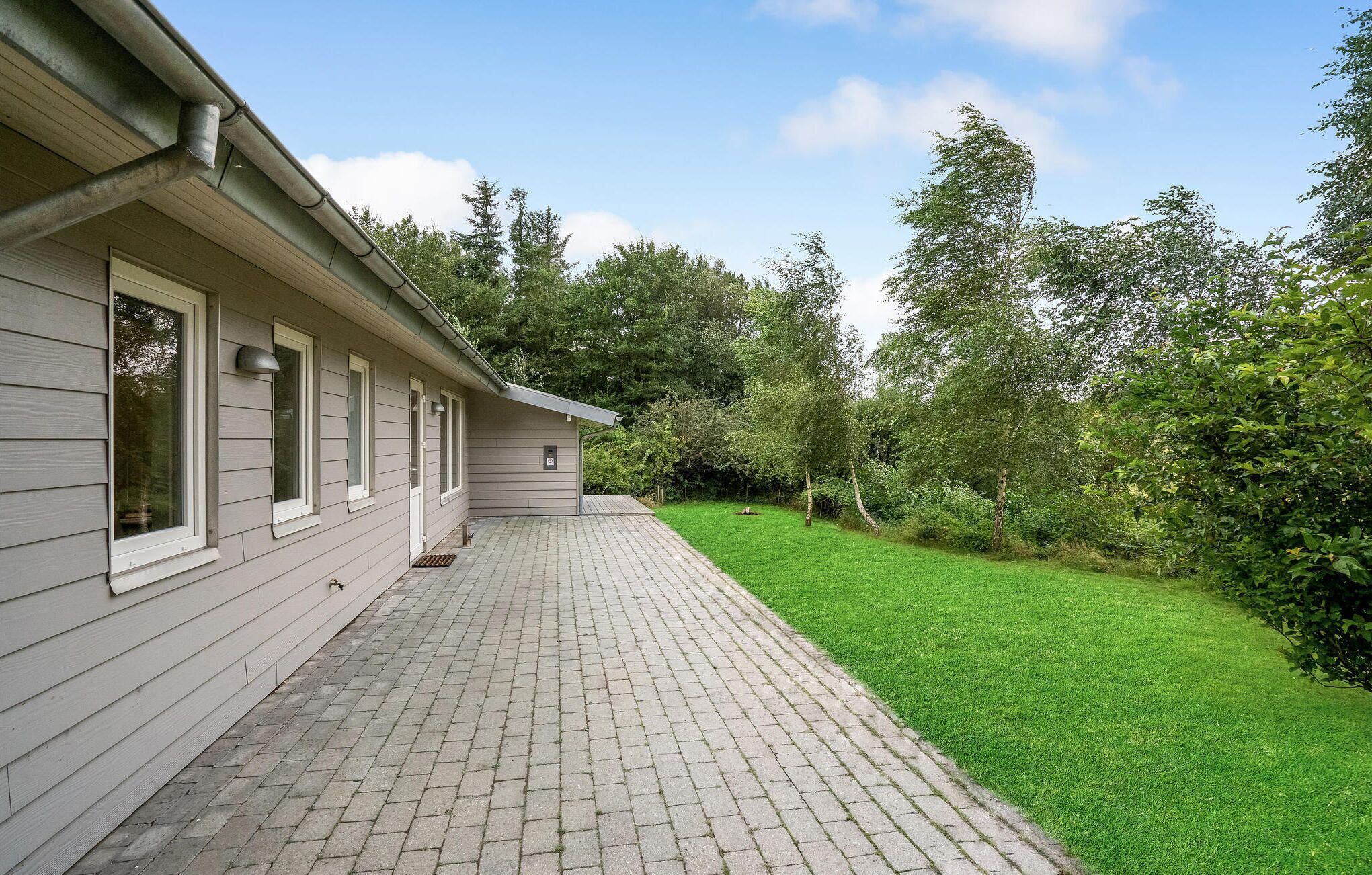 Une maison avec une terrasse dallée et une cour gazonnée.