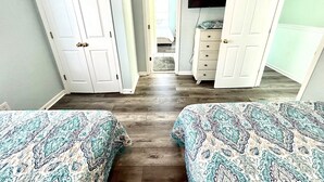 A bedroom with two beds, a dresser, a television, and a door leading to another room.