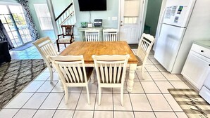 A dining area with a wooden table and white chairs, a kitchen with white cabinets and appliances, and a TV mounted on the wall.