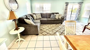 A living room with a sectional sofa, a small table, a lamp, and a ceiling fan.