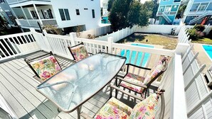 A deck with a glass-top table and floral-patterned chairs, surrounded by a white fence.