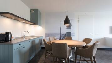 A modern kitchen with a dining area, featuring a large island, pendant lighting, and a view of the sea.