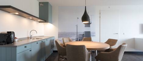 A modern kitchen with a dining area, featuring a large island, pendant lighting, and a view of the sea.