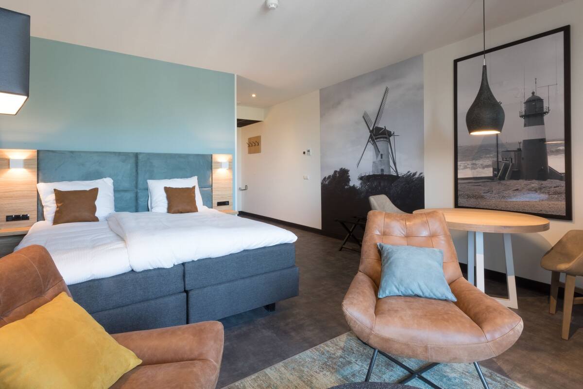 Une chambre d’hôtel moderne avec un grand lit, un canapé, un fauteuil et une table.