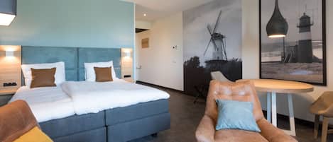 A modern hotel room with a large bed, a sofa, a chair, and a table.