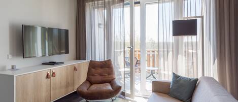 A modern living room with a sofa, a brown leather chair, a flat-screen TV, and a sliding glass door leading to an outdoor area.