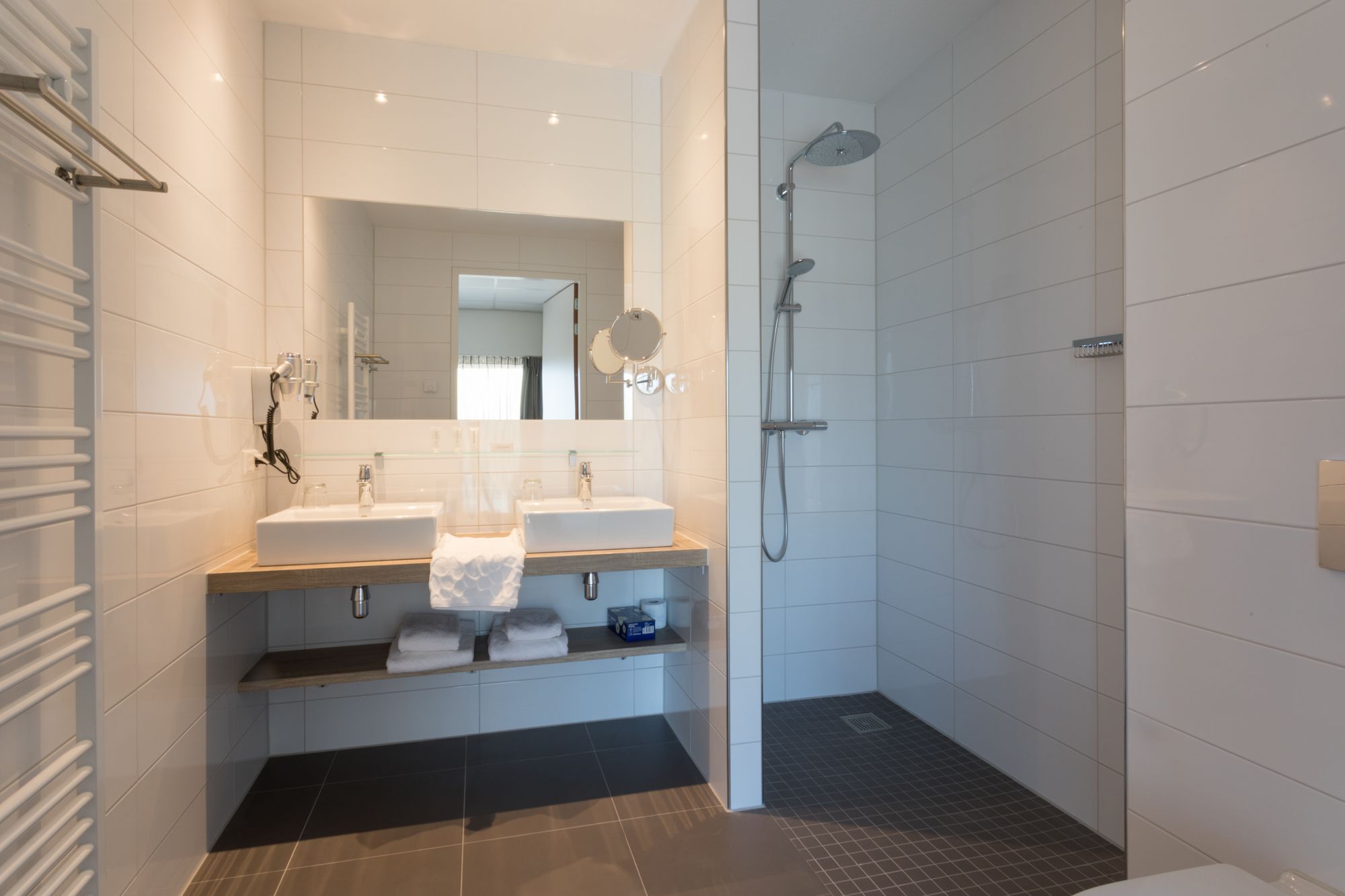 A modern bathroom with two sinks, a mirror, a shower, and a towel rack.