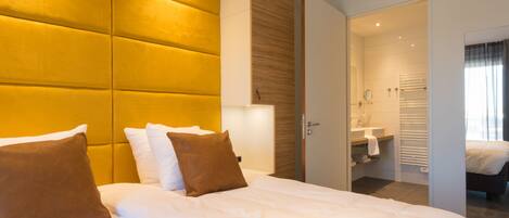 Una habitación de hotel con una cama grande, una mesita de noche, un espejo y un baño visible a través de una puerta abierta.