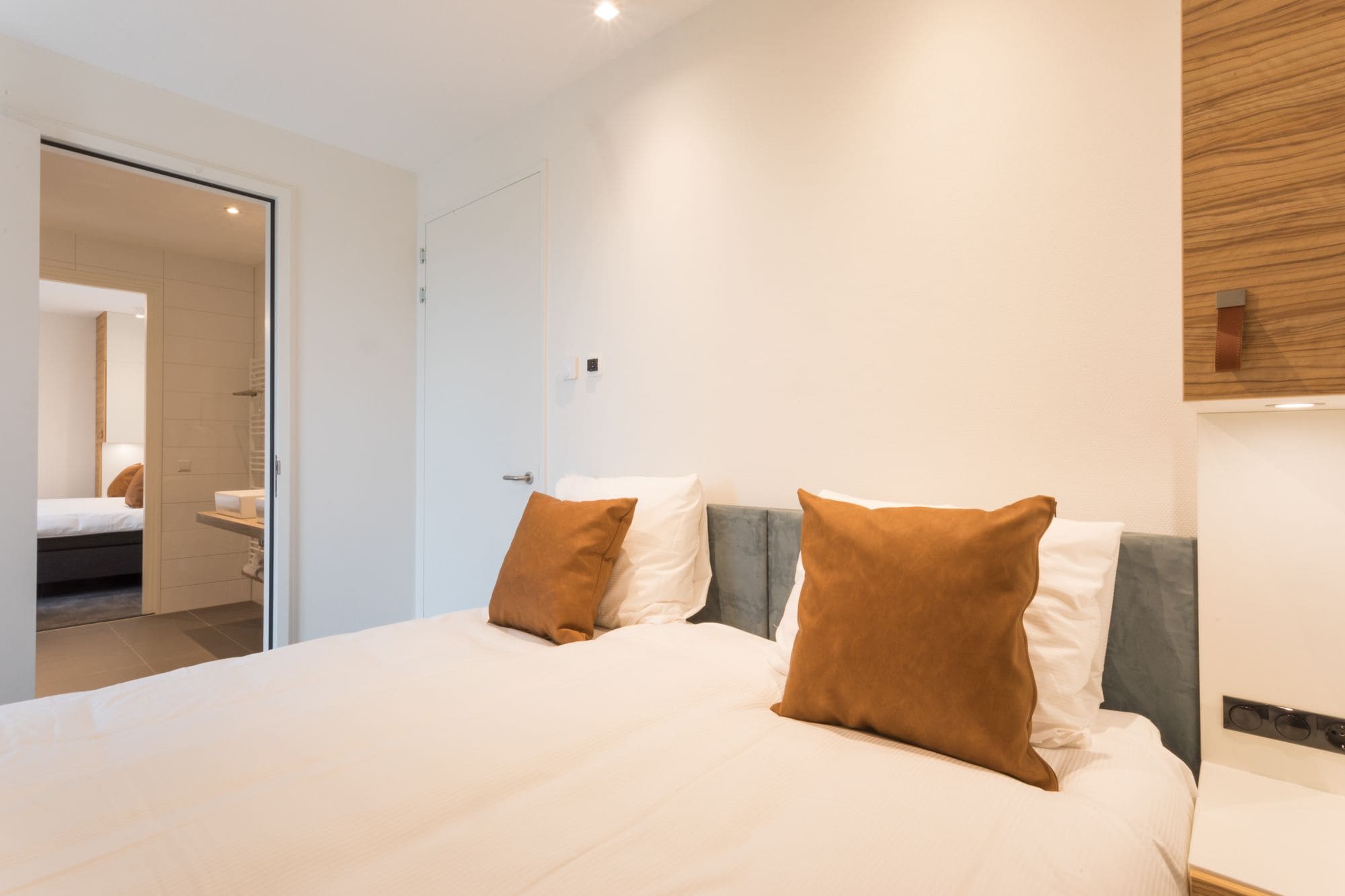 A modern hotel room with a large bed, two pillows, a bedside table, and a wooden accent wall.