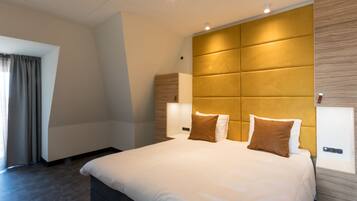 A modern hotel room with a large bed, a wooden headboard, and a nightstand with a lamp.