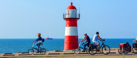A coastal scene with a red and white lighthouse, a paved walkway, and a calm sea with a ship in the distance.
