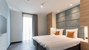 Ein modernes Hotelzimmer mit einem großen Bett, einer fest eingebauten Kopfteil und einem großen Fenster mit Vorhängen.