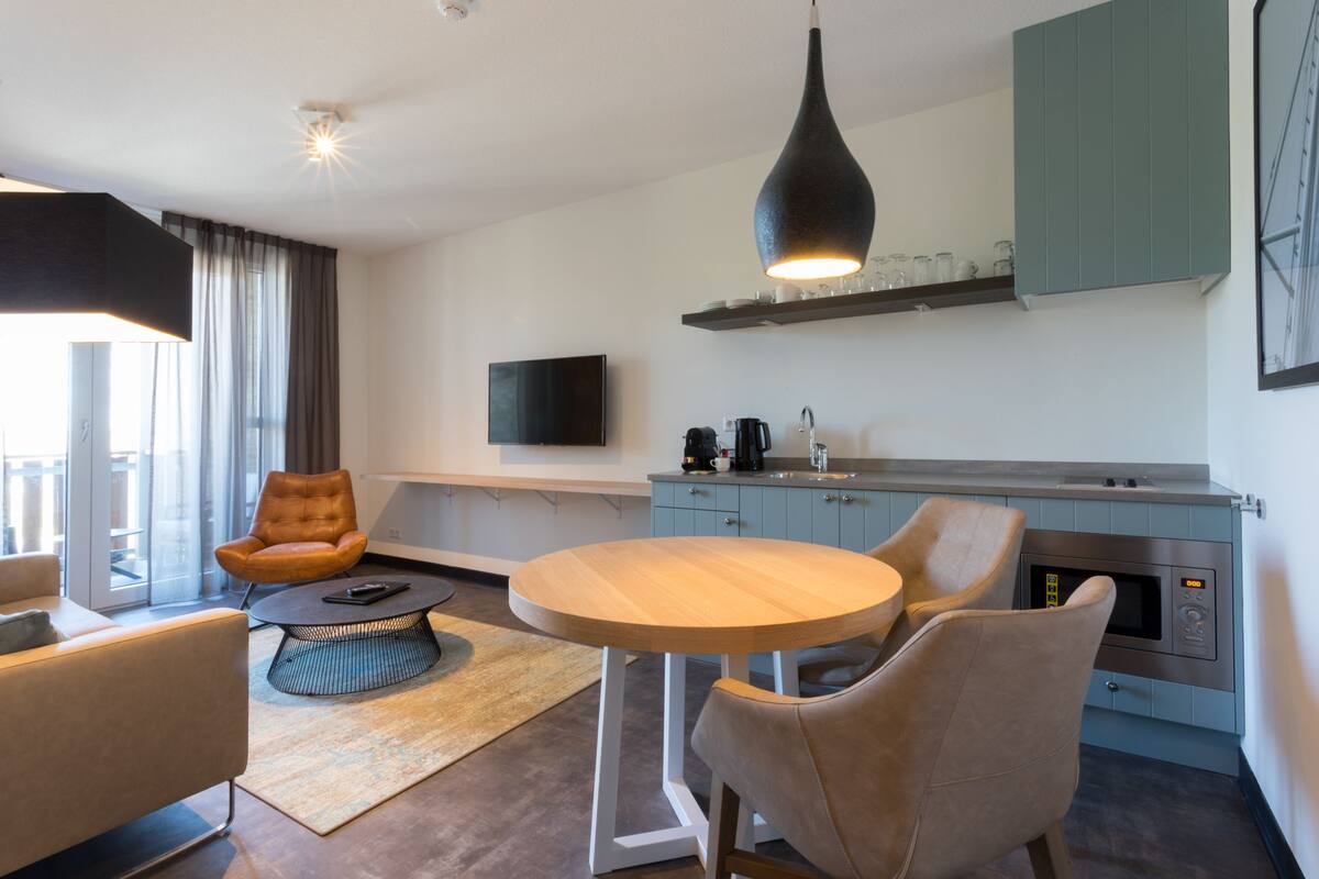 Une cuisine moderne avec une table de salle à manger ronde, deux chaises, une machine à café et un téléviseur fixé au mur.