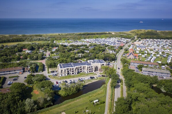 Luchtbeeld van een kustgebied met woonhuizen, een groot gebouw met zonnepanelen, omringd door groen en water.