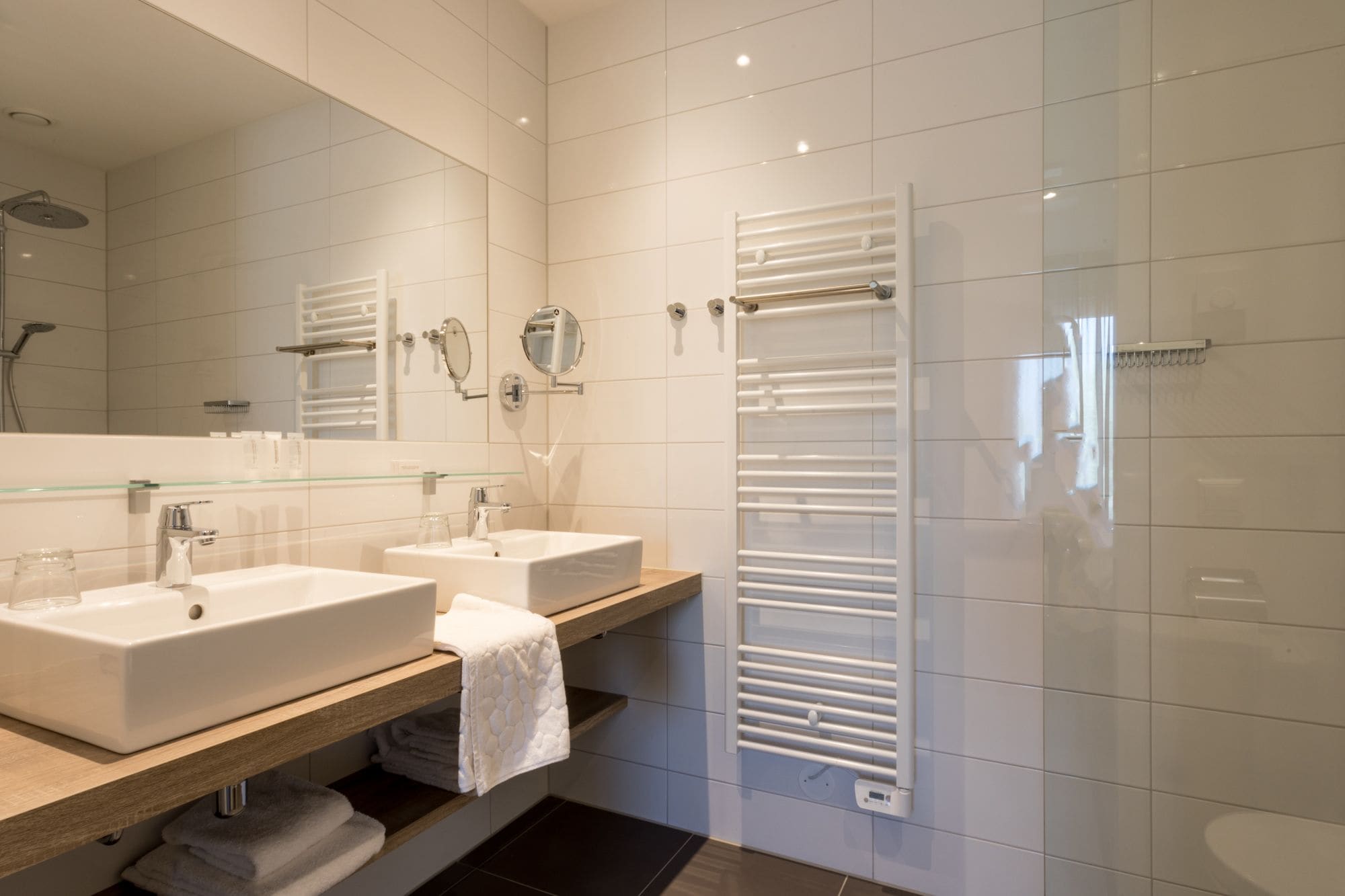 A modern bathroom with two sinks, a glass shower enclosure, and a white towel rack.