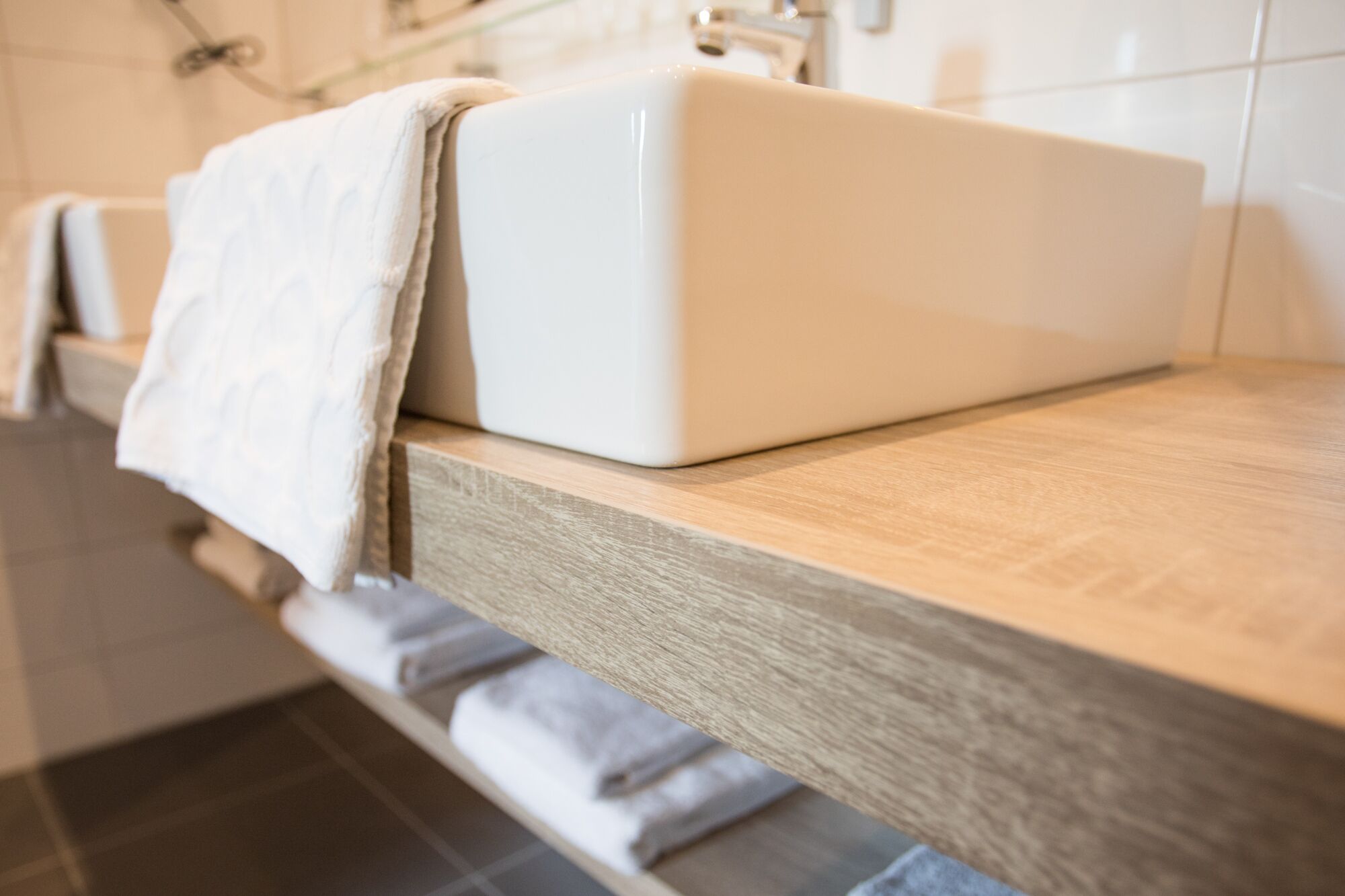 Une salle de bain avec un lavabo blanc, un plan de toilette en bois et une serviette accrochée sur le côté.