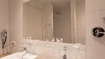 Une salle de bain moderne avec deux lavabos, une étagère en verre où sont rangés les articles de toilette, un grand miroir et un espace douche.