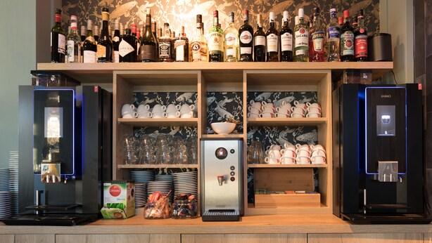 Un espace bar avec un assortiment de bouteilles d’alcool, un appareil à café et des étagères remplies de tasses et d’assiettes.