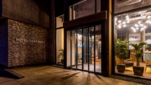 L’entrée d’un hôtel, avec une façade en briques, des portes en verre et des plantes en pot.