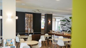Un café moderno con mesas redondas y sillas blancas, una pared decorativa y una barra con frascos de aperitivos.