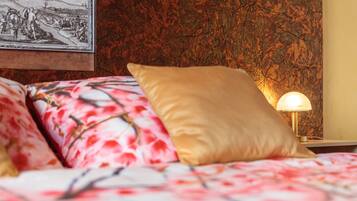 Un lit avec une literie à motifs floraux et un oreiller doré, un tableau accroché au mur et une table de chevet avec une lampe.