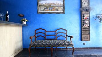 A blue wall with a framed painting, a wooden bench, a shelf with decorative items, and a vertical display of postcards.