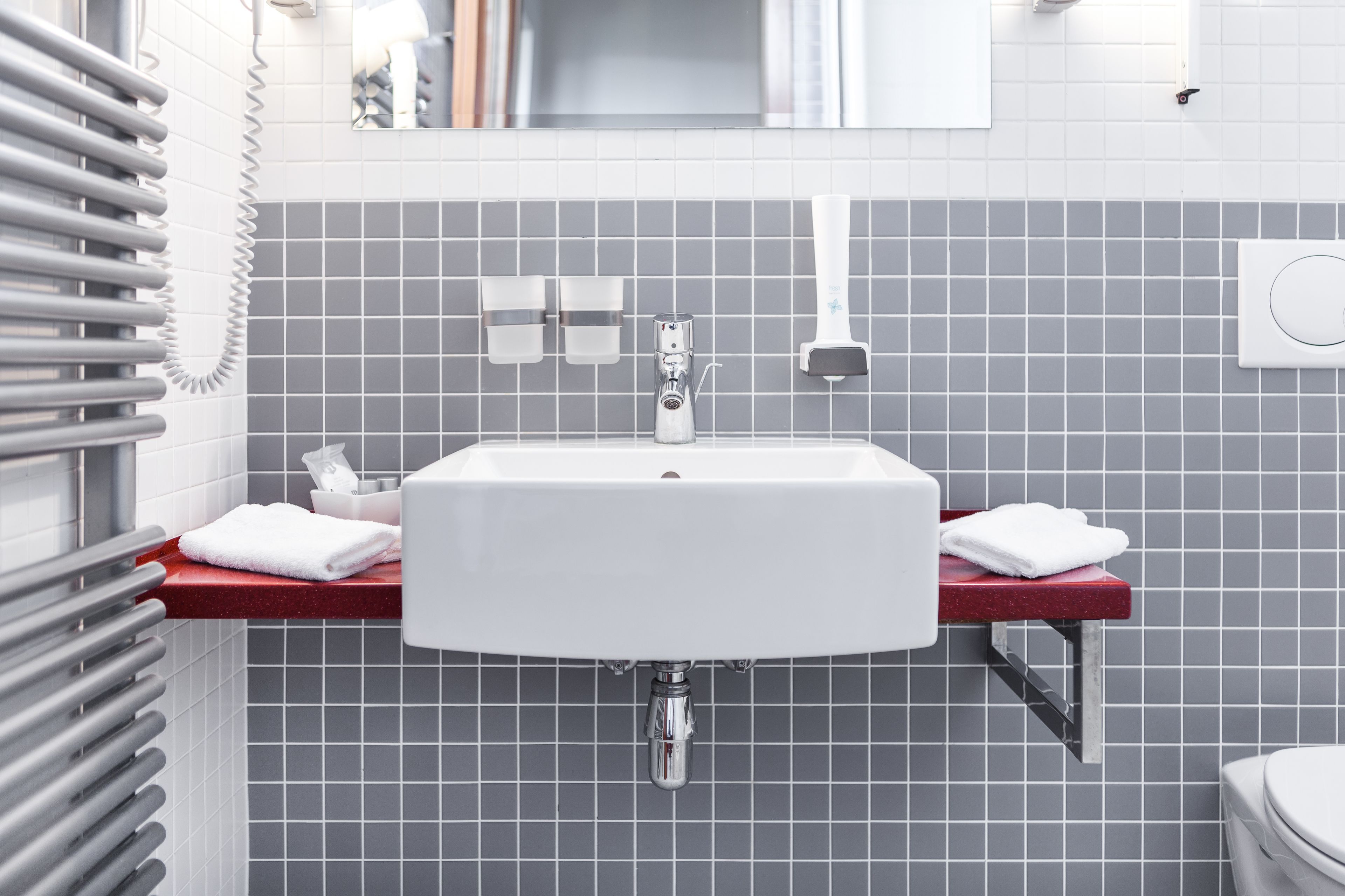 Un baño con lavamanos blanco, encimera roja y paredes cubiertas de baldosas grises.