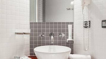 Un baño con lavamanos blanco, espejo, secador de pelo y toallero.