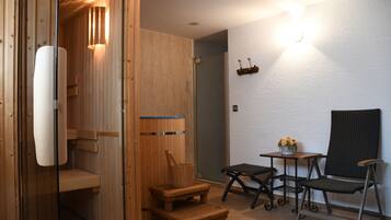 A wooden sauna room with a bench, a small table with a vase, and a chair.