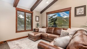 A spacious living room with a brown leather sectional sofa, large windows offering mountain views, and a wooden ceiling. - Breiding Upper Luxury Vacation At Windcliff 2 Bedroom Home by RedAwning (Estes Park)