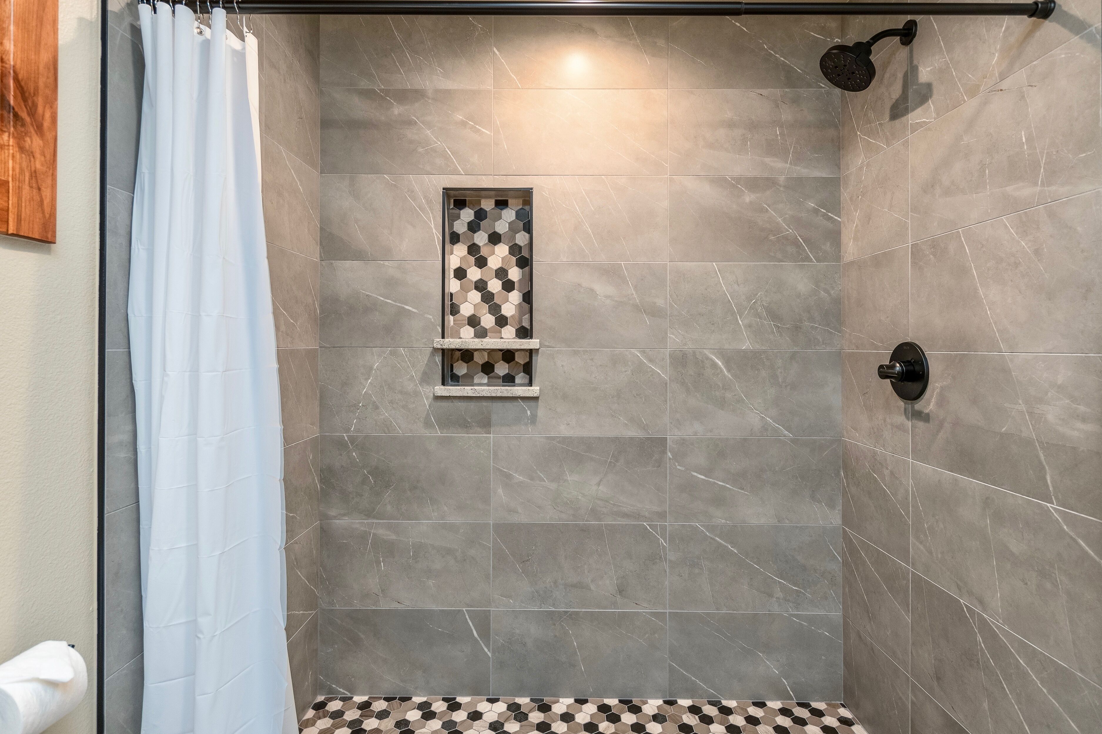 A shower area with a tiled floor, a showerhead, and a window with a geometric pattern.